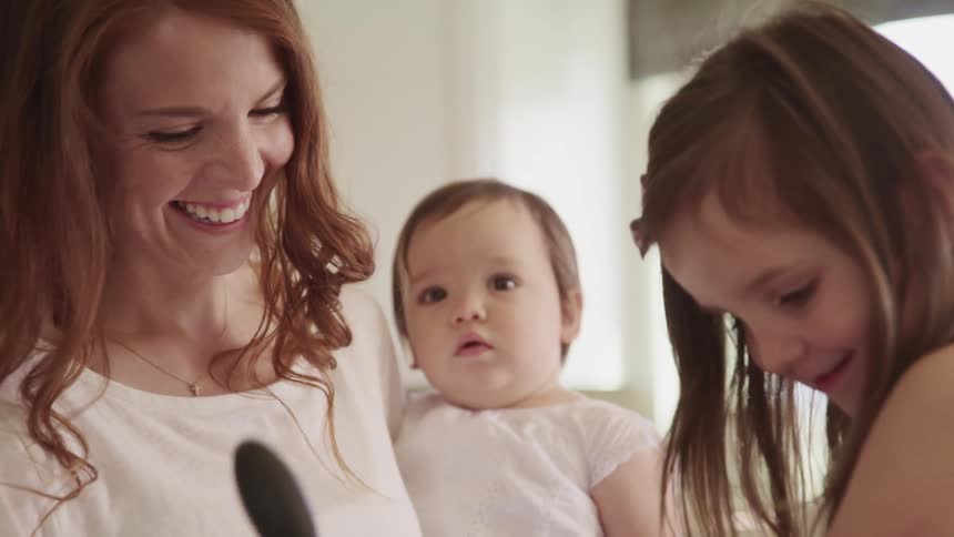 Mother smiles and laughs while holding a baby as a young girl is next to her