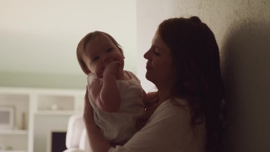 Mother holding and kissing a baby on her arms at home