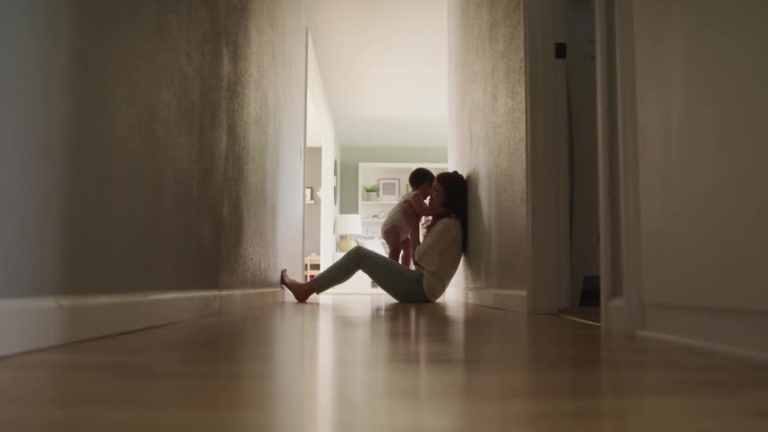A woman sits on the floor at home and holds her baby in her lap