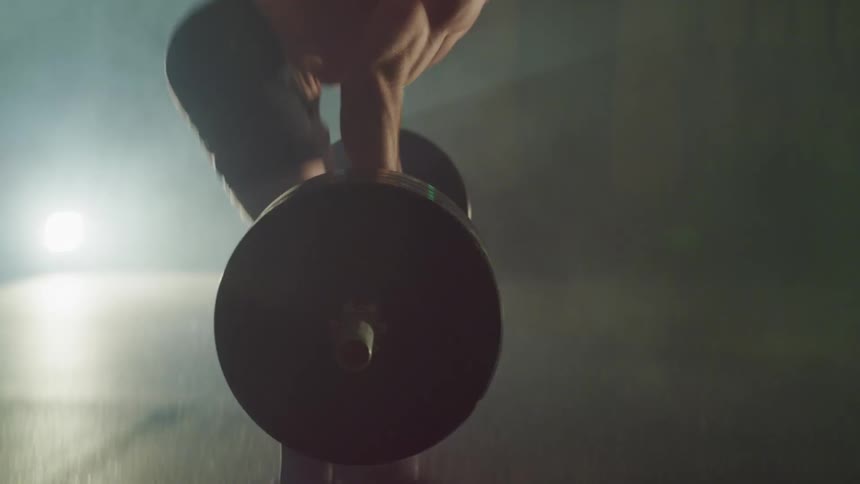 Bare chested man lifts heavy weight bar in foggy room