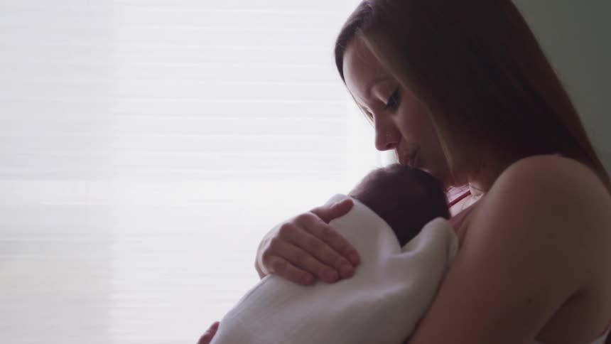 Mother with brown hair holds a baby and kisses his forehead