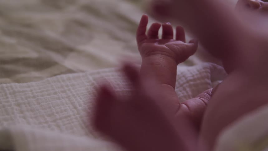 An infant rolls around on a bed while biting its hand