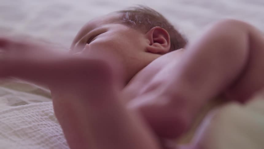 A baby cries while laying on a bed sheet
