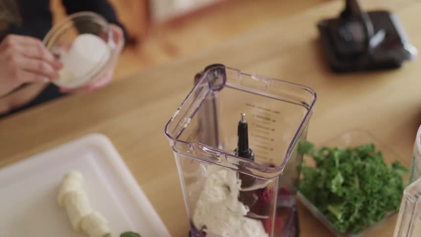 A woman pours powder into a blender filled with cream and berries