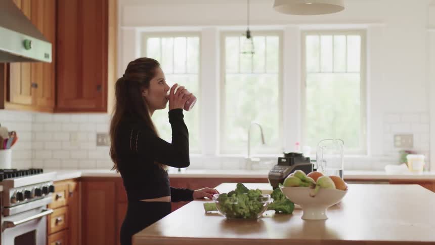 Woman drink a glass of fruit juice over the counter on the kitchen at home