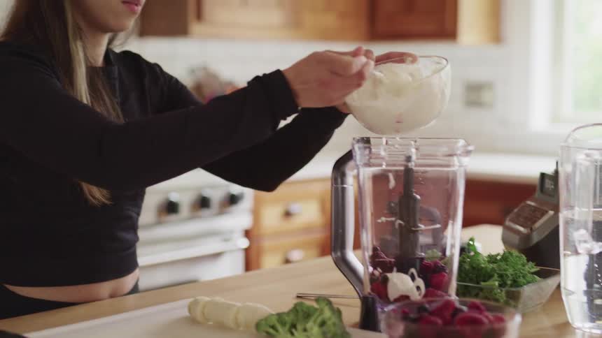 Spooning a creamy mixture into a blender over strawberries