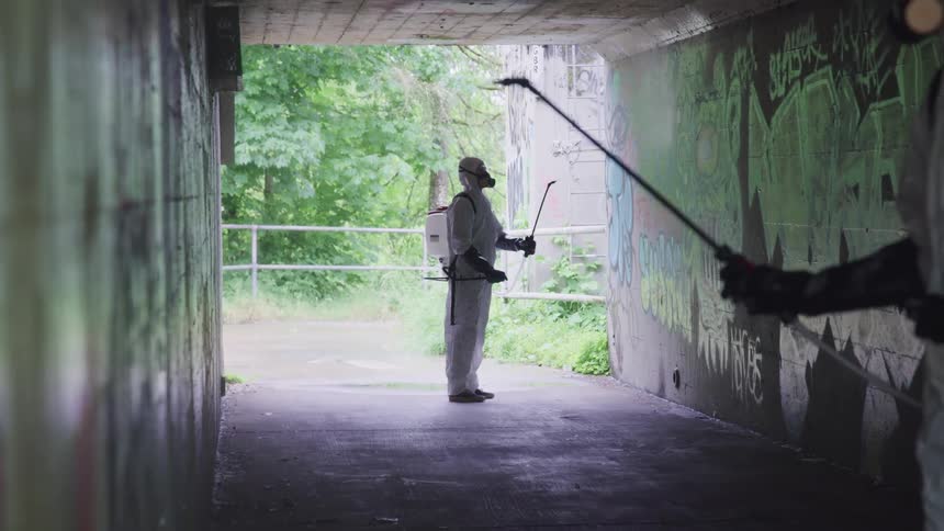 People wearing protective gear use a sprayer on graffiti inside a tunnel
