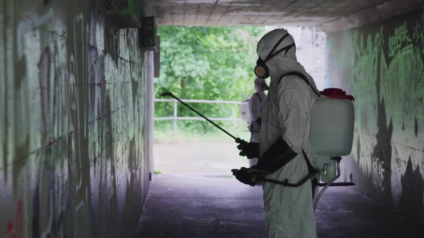Two people use a paint sprayer to cover graffiti in a tunnel
