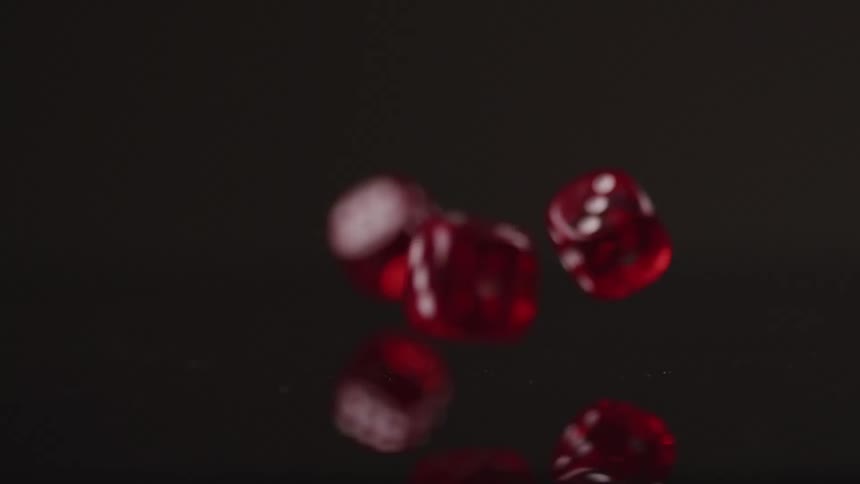 Several transparent red dice fall onto a reflective surface and bounce for a moment before coming to a stop