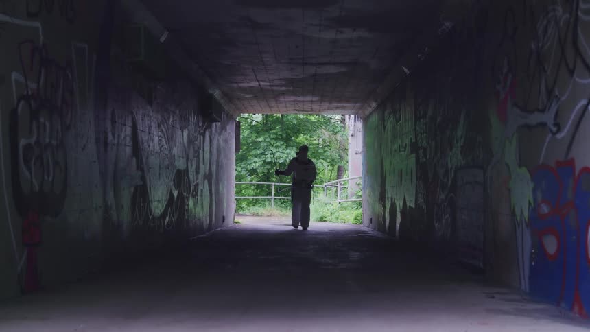 A person in a respirator and coveralls sprays chemicals on the walls of a concrete tunnel