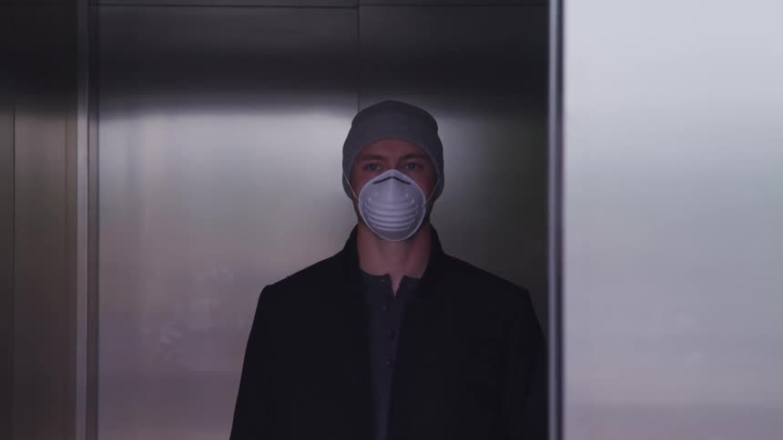 A man in a dust mask stands in an elevator looking towards the camera as the elevator door closes