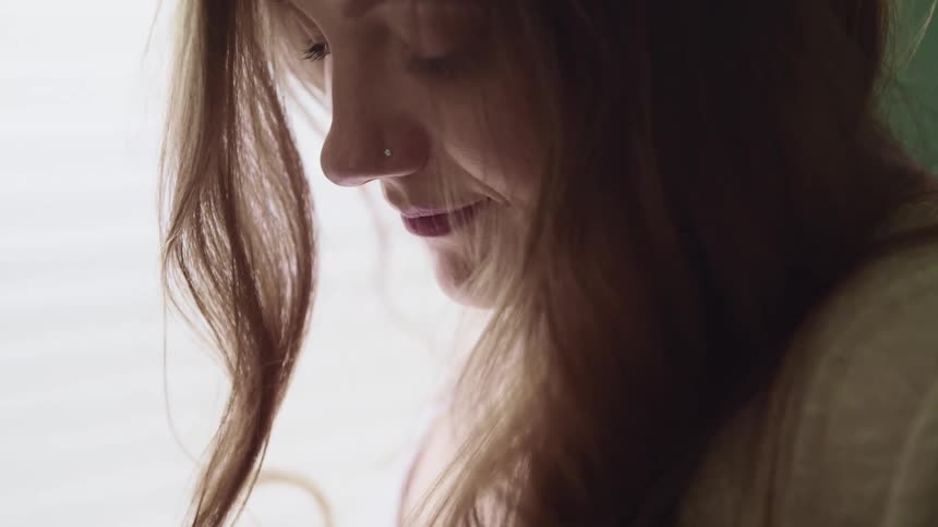 Close up of a long haired womans face in a room next to the window
