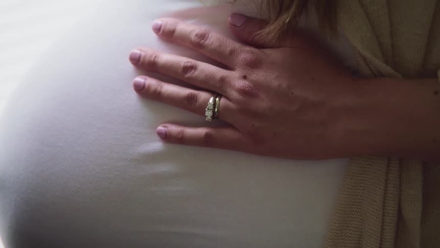 Pregnant woman wearing wedding ring holds her belly
