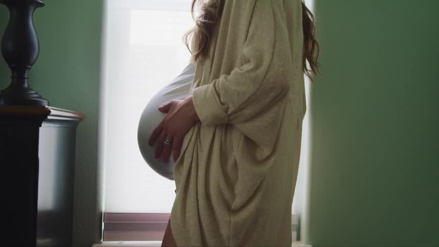 Pregnant woman wearing a robe at home rubs her belly