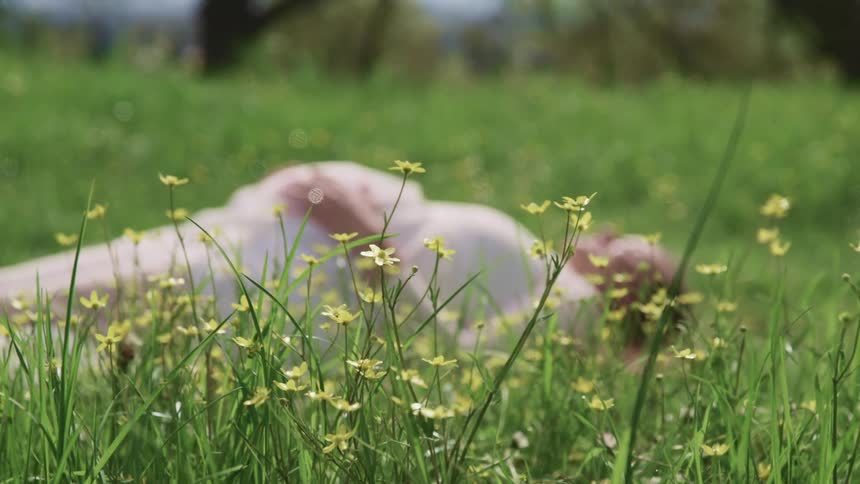 Pregnant woman with a white dress lies down on the green grass and holds her belly on a sunny day