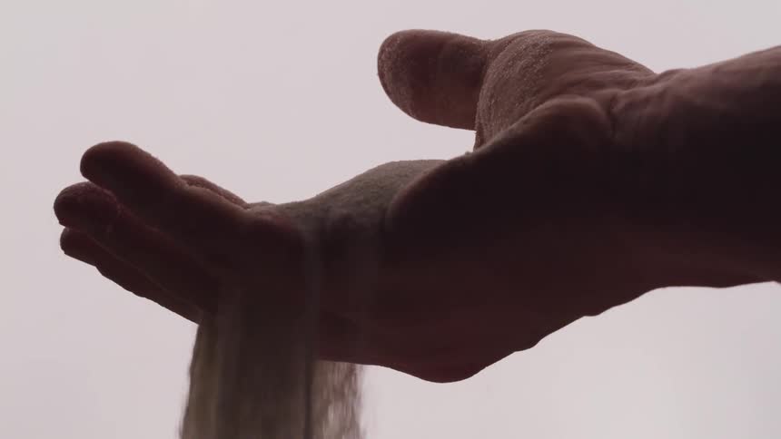 A person slowly drops a handful of sand