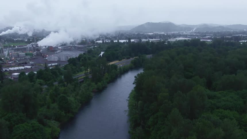 The smoke rises from the factory by the river