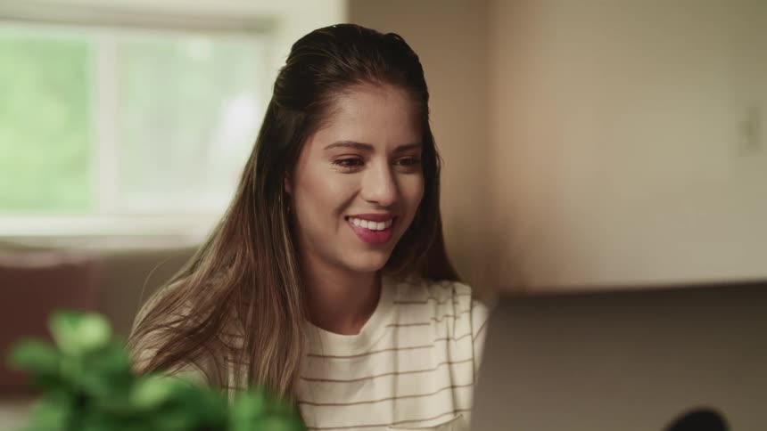 A young woman smiles while using a laptop in a house during the day