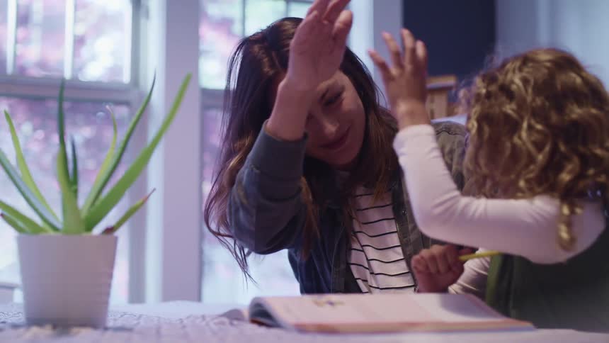 Mother and daughter high five each other while making homework on a table at home