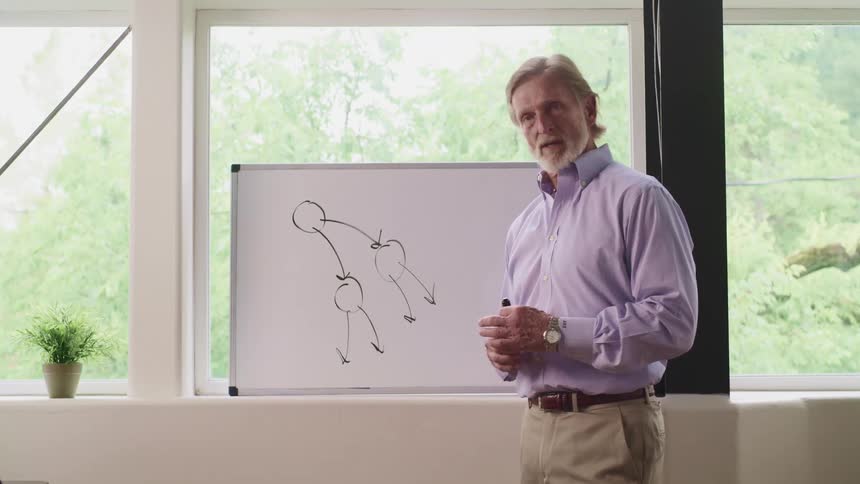 A man is teaching something while pointing towards a whiteboard