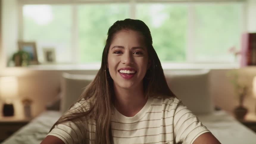 Brunette woman with brown straight hair and a white t shirt talks to the camera