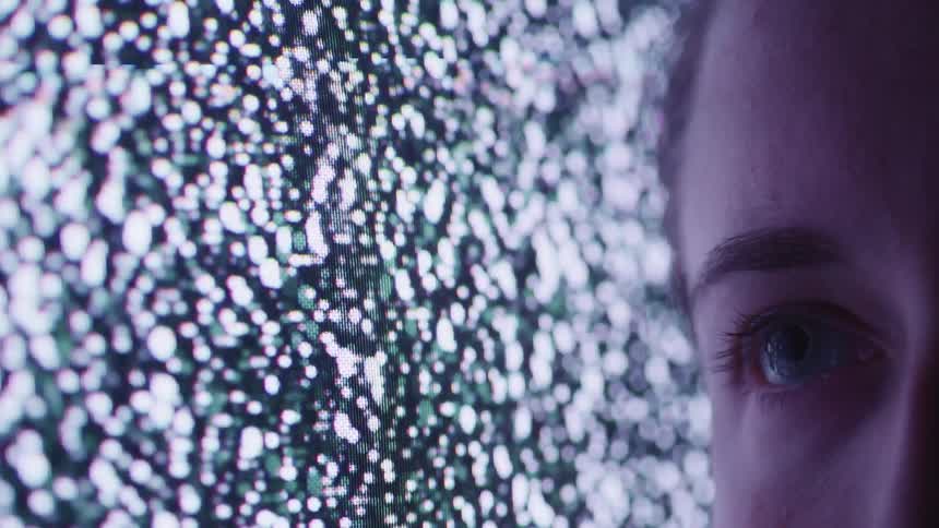 Close up of a womans eye against a tv screen showing static