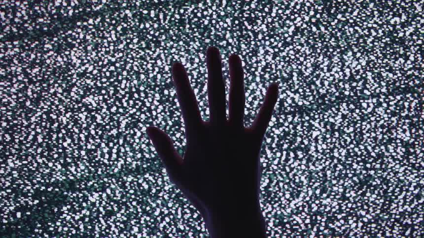 Silhouette of a hand slowly touching a television screen showing static
