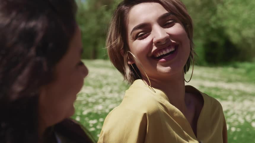 Two young women sit in the grass laughing