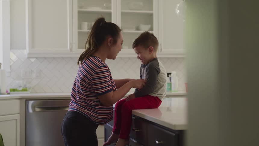 Mother plays with son sitting on kitchen counter