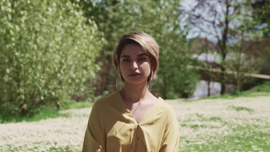 A young indian woman standing in a meadow looks into the camera