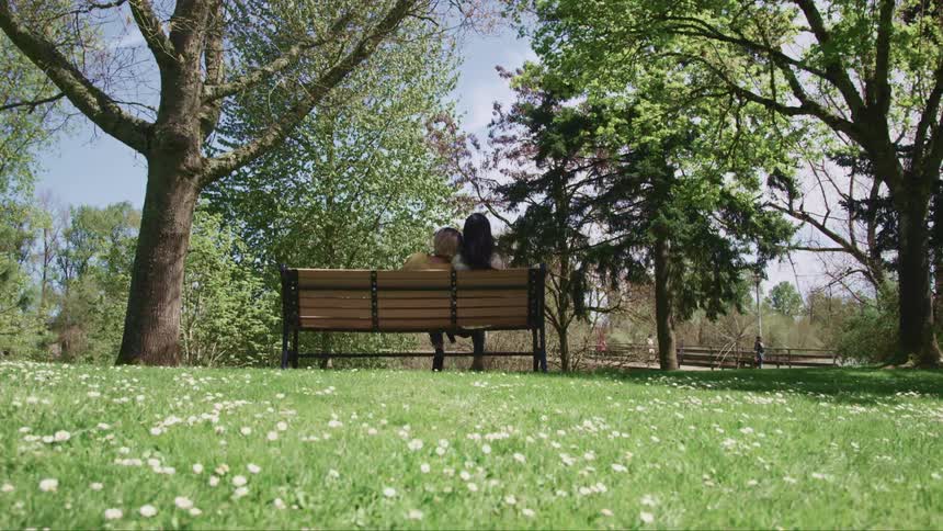 Two women sit down on a park bench in a public garden