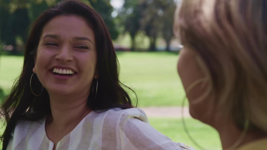 Two women laugh as they sit and chat in a park