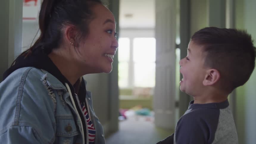 A mother kneels down close to her son and make funny faces at each other