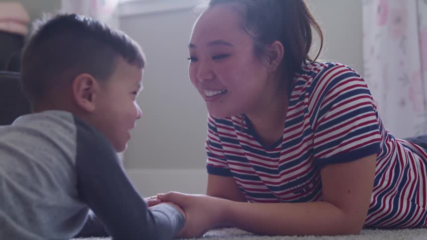 Mother and son hold hands laying on the carpet in a room at home