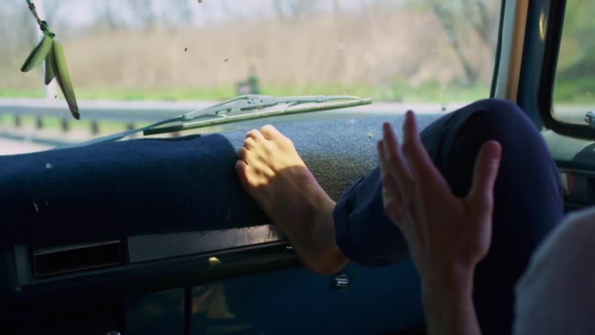 A white person rides shotgun with their foot on the dashboard