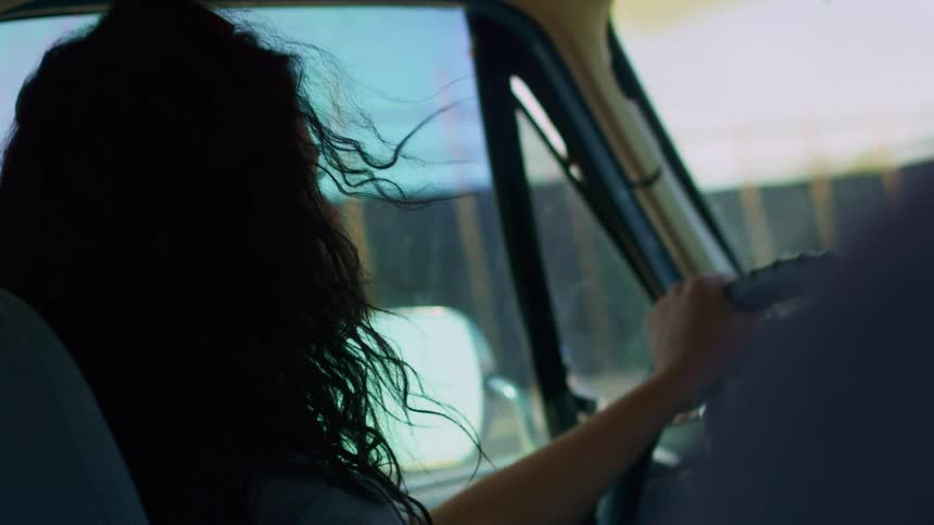A dark haired woman drives a vehicle down a street