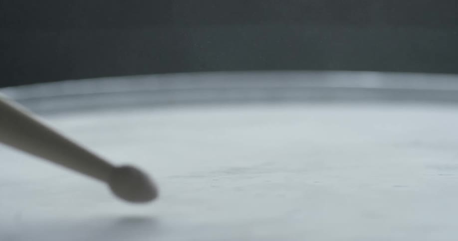 A drumstick is tapping on a drum in daylight