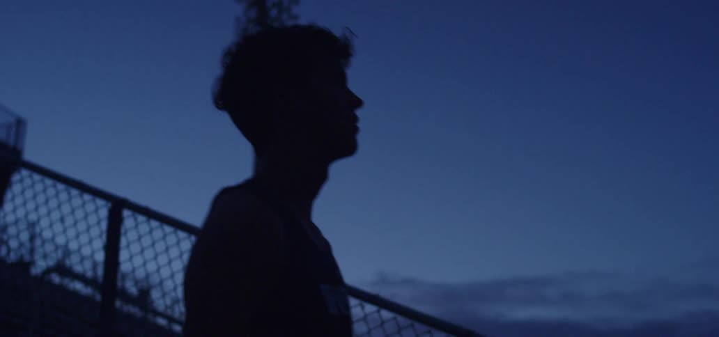 A teenage athlete stands in a stadium at night