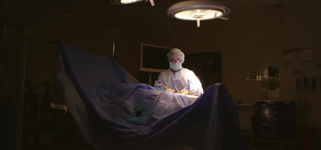 A surgeon operates on a patient alone in a dimly lit operating room