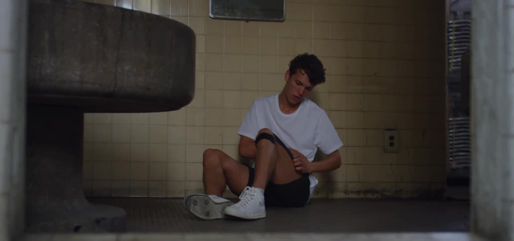 A teenager sits on the floor and rubs his leg