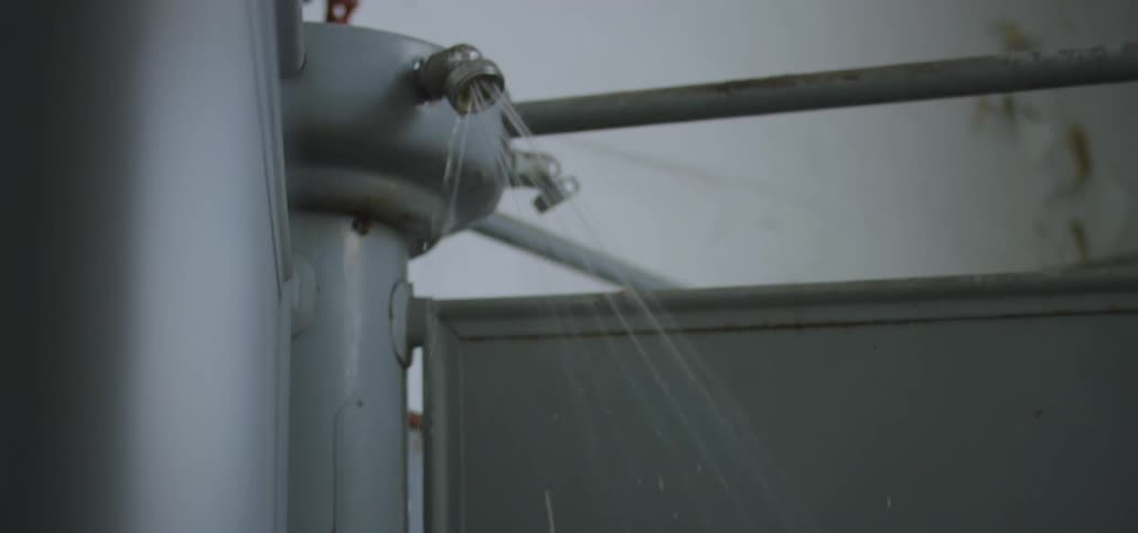A persons hand turning a valve as water comes out of a showerhead with the sky in the background