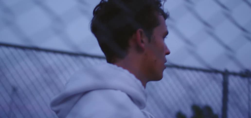 A young man in a white hoodie walks between two rows of chain link fences