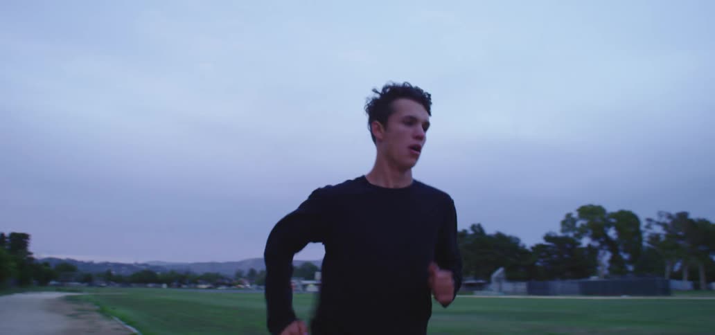 A young man runs along a dirt path around a field in a small town