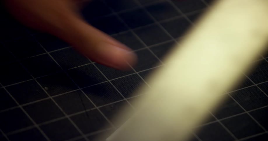 Man measures and cuts over a piece of paper using a cutting knife and a metallic ruler