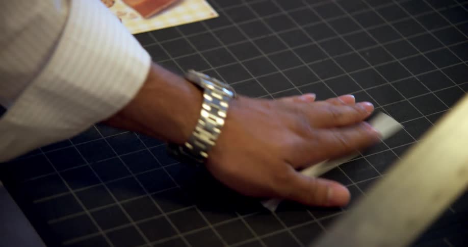 A man uses a utility knife to trim a brochure on a craft mat