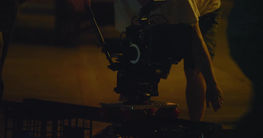 Man moves a video camera as someone walks by pushing a shopping cart at night