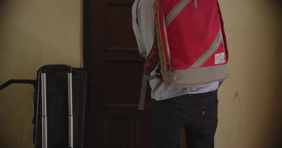 Man carrying backpack locks door before leaving with luggage