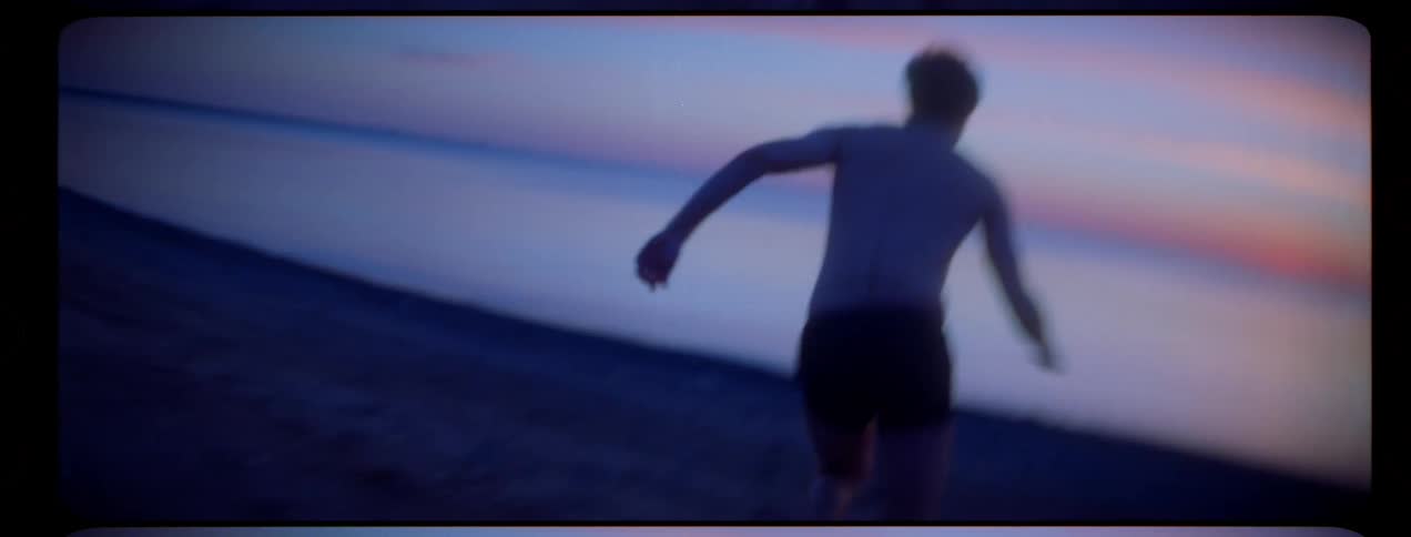 A man in the beach running on sand towards the water with the sky and clouds in the background