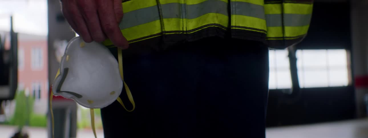 A firefighter holds a dust mask in his hand as he stands by the open garage of a firehouse