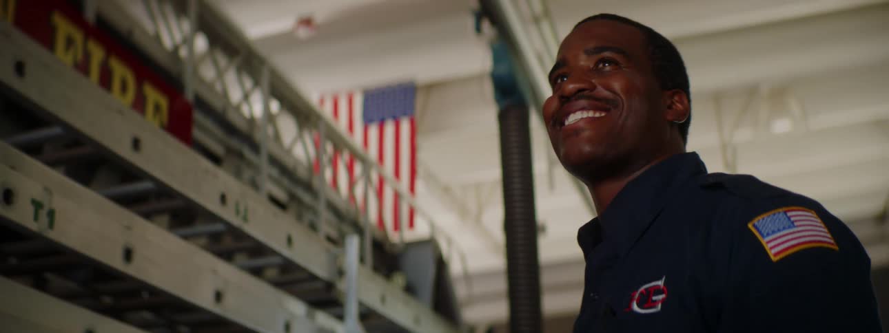 A man in a uniform in a fire station next to a fire truck with an american flag in the background